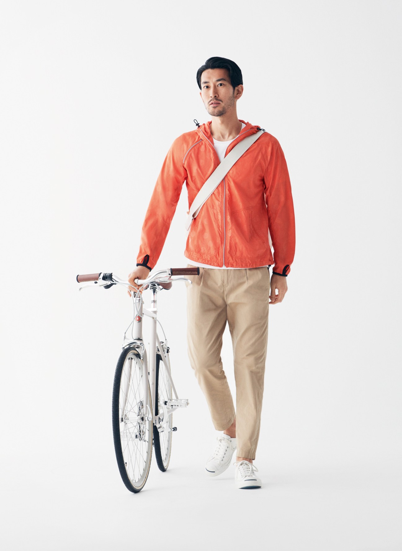 Man in red jacket and beige trousers holding a white Tokyobike bicycle.