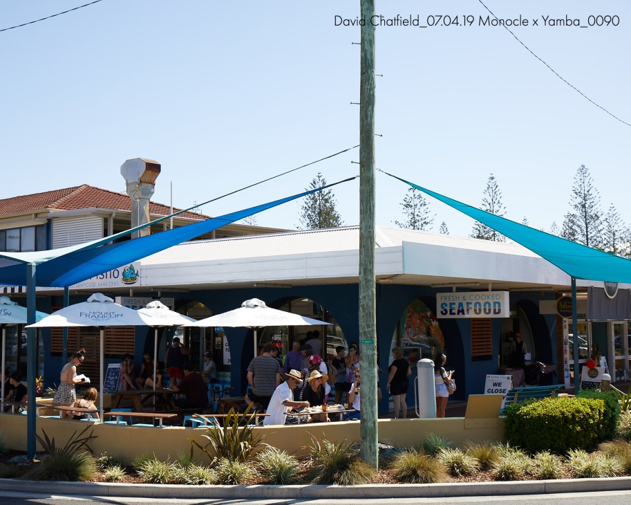 A beachside seafood restaurant with blue awnings and white umbrellas, displaying a fresh fish catch on ice.