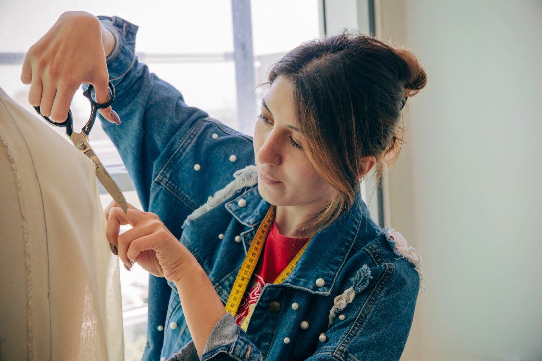 Fashion student measuring fabric with a measuring tape while working on a garment.