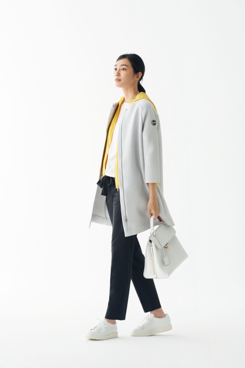 Woman in Colmar jacket, Red Valentino hoody, and Salvatore Ferragamo bag standing against white background.