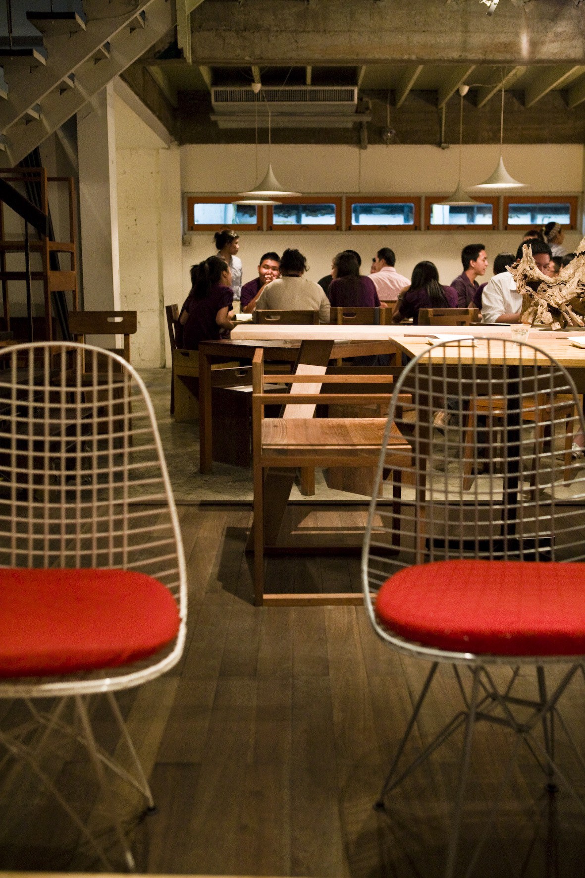 Interior of PlaDib restaurant with diners seated at long wooden tables under pendant lights.