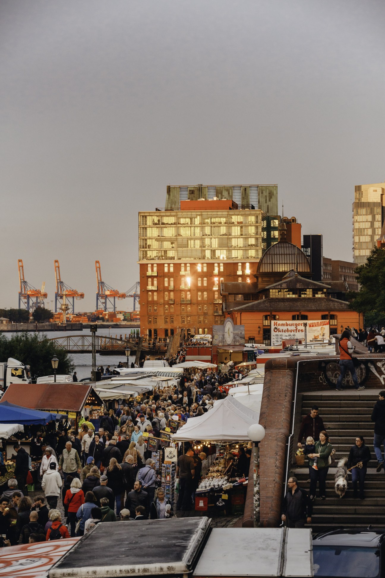Aerial view of Hamburg Fish Market on a busy Sunday morning with crowds, market stalls, and harbor cranes in background.
