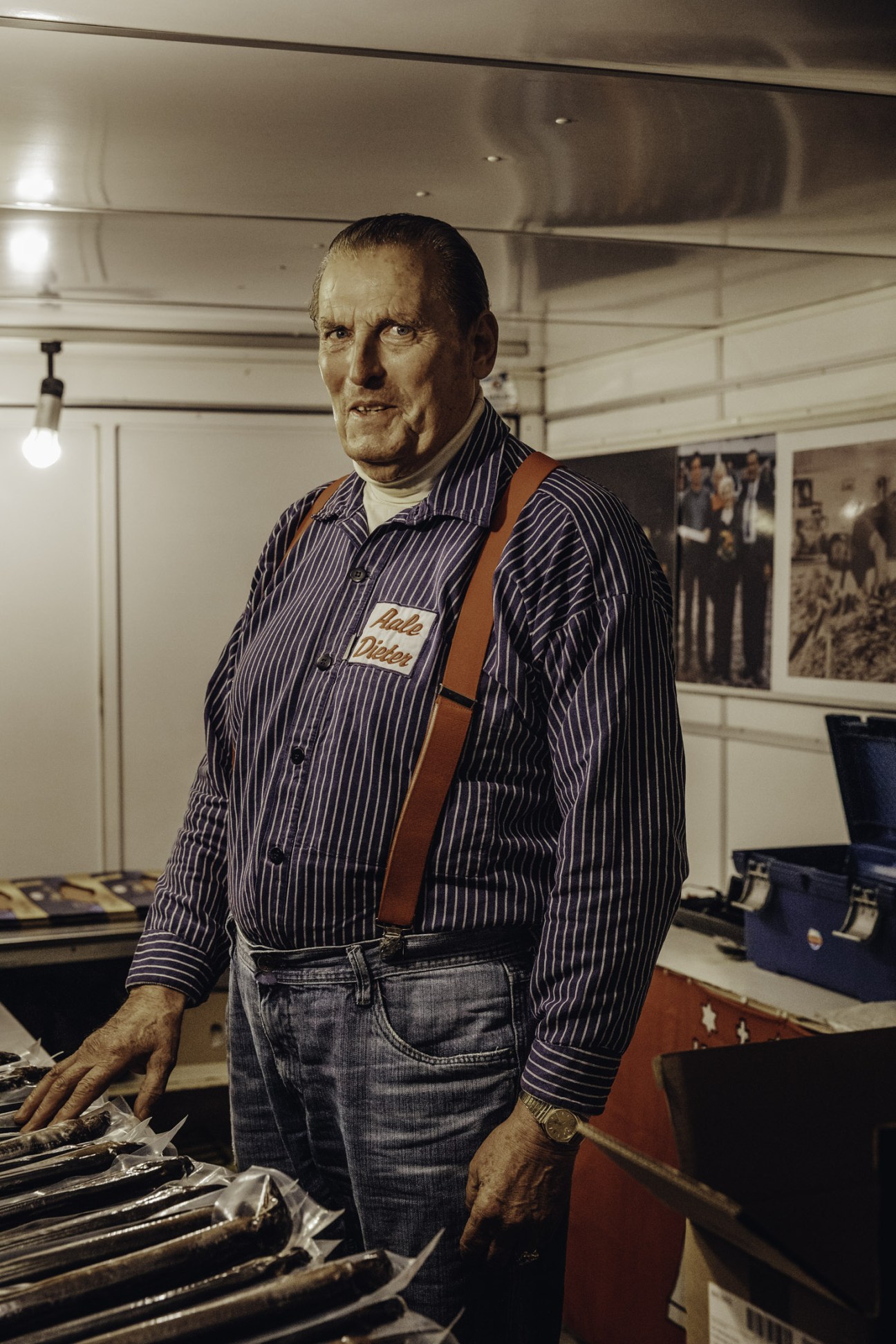Stall owner 'Aale Dieter' (Eel Dieter) in pinstriped shirt and brown apron waiting for first customers at Hamburg Fish Market.