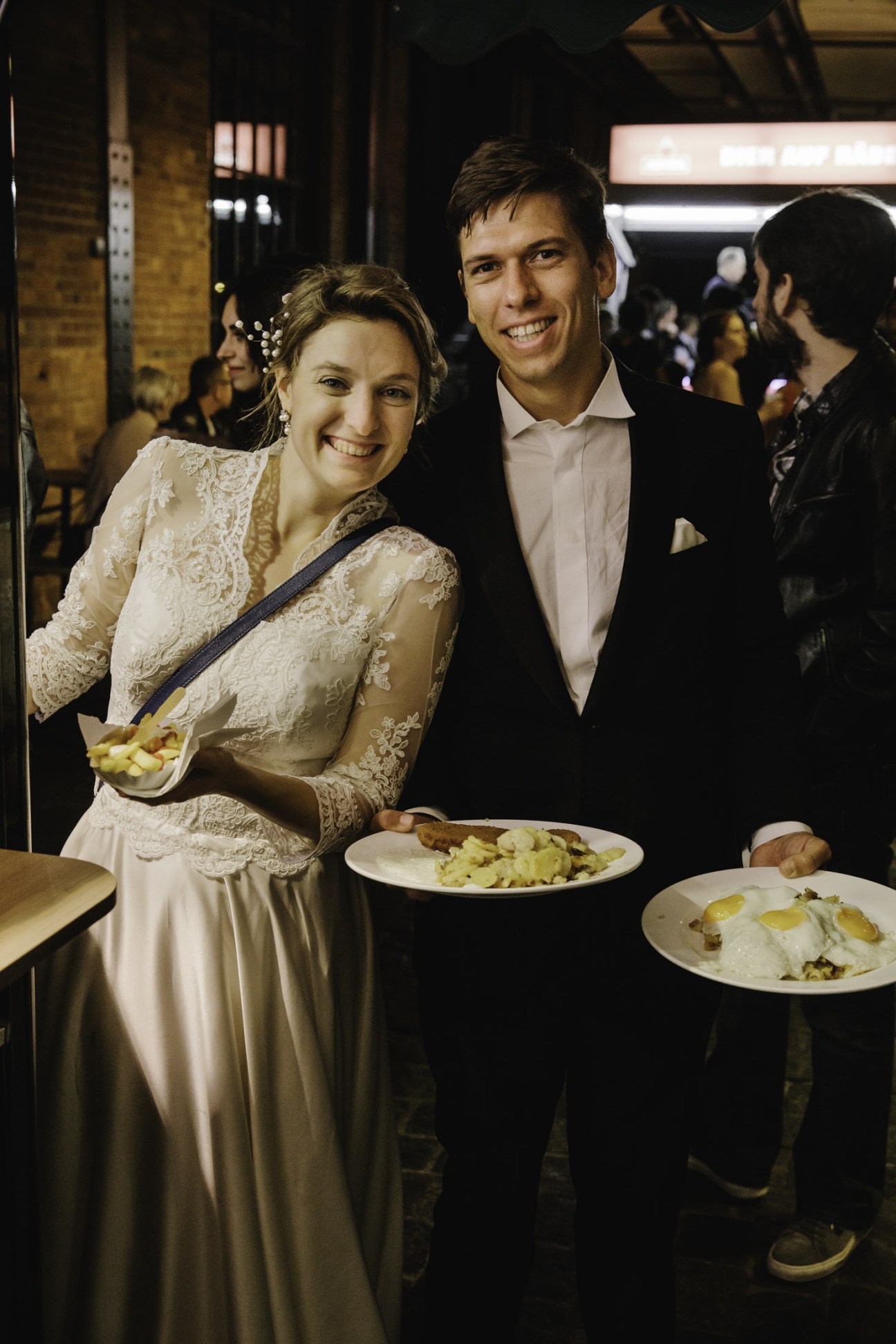 Newlyweds in formal attire holding plates of food at Hamburg Fish Market