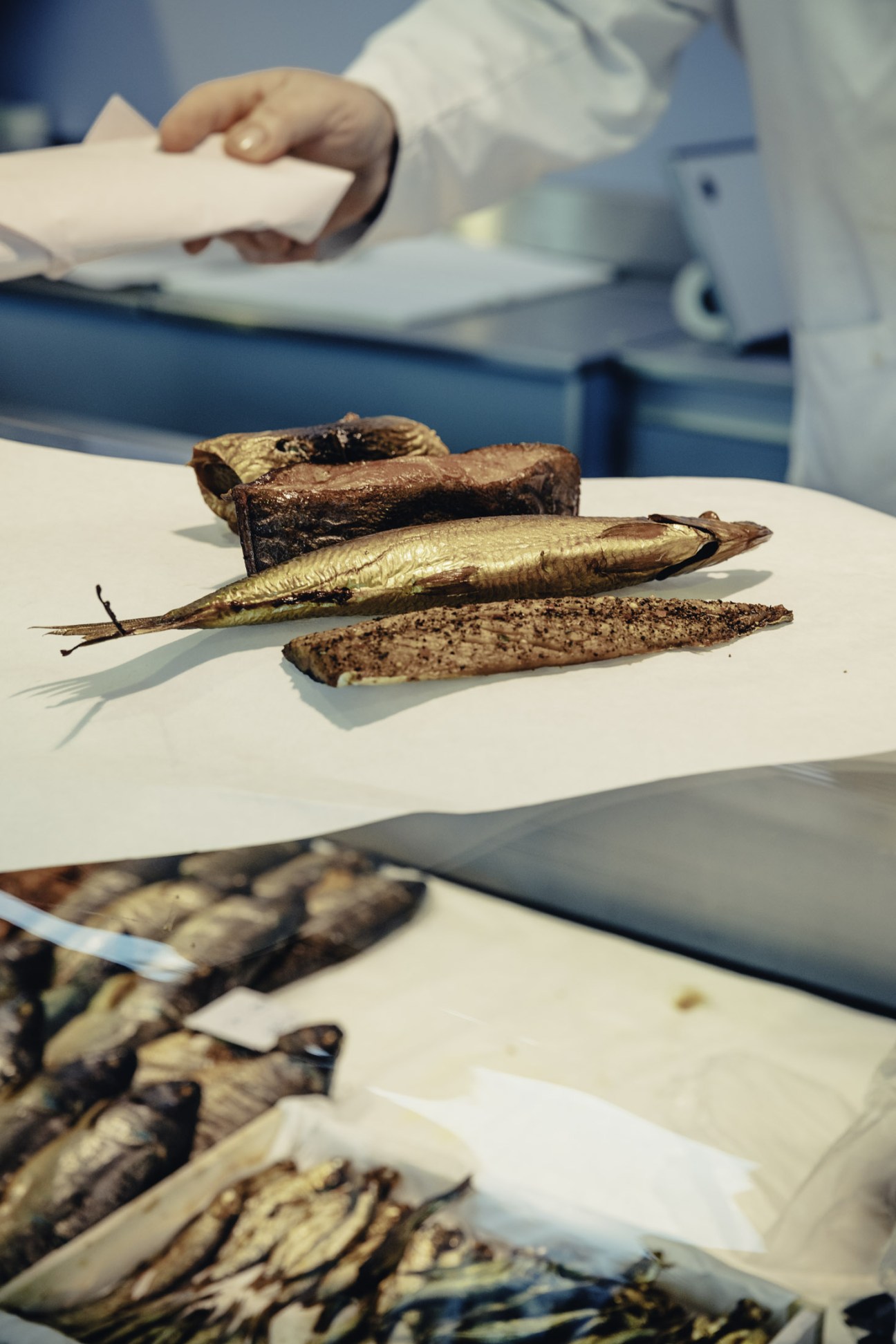 Smoked fish displayed on white paper at Hamburg Fish Market with vendor's hands visible.