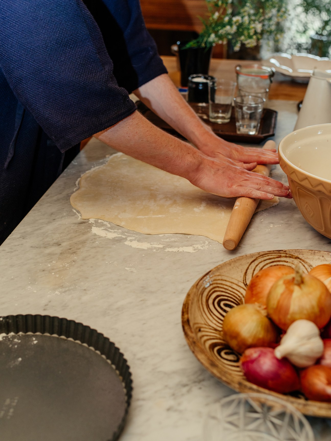 Hands rolling out pastry dough with a wooden rolling pin on a floured surface