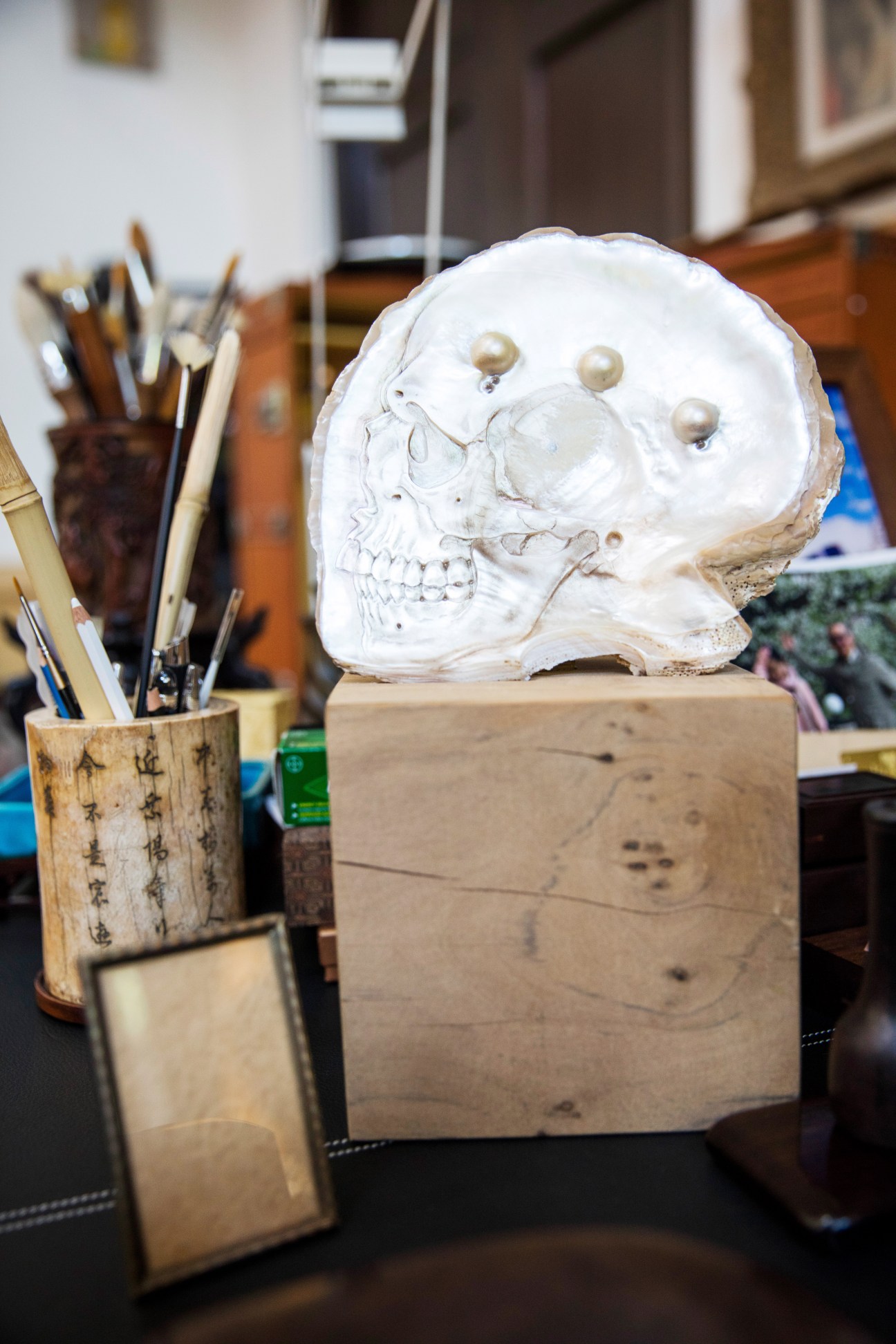 White plaster skull sculpture with pearl eyes on wooden base in artist studio with paintbrushes