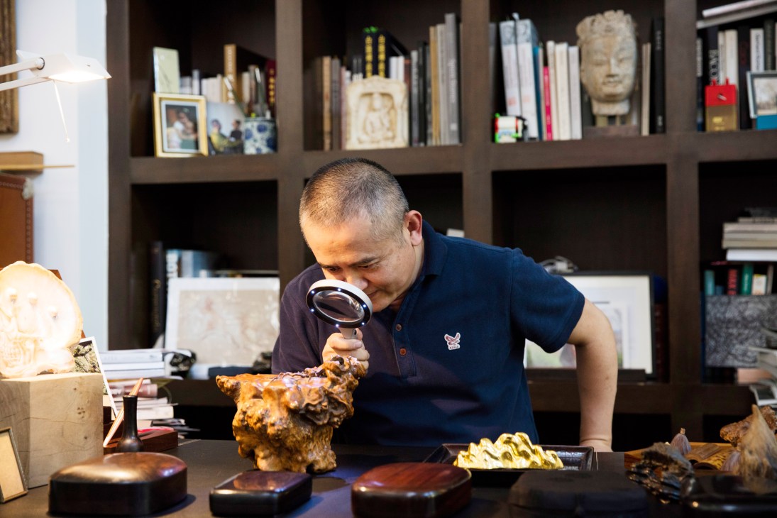 Artist Zeng Fanzhi examines a small sculpture through a magnifying glass in his Beijing studio.