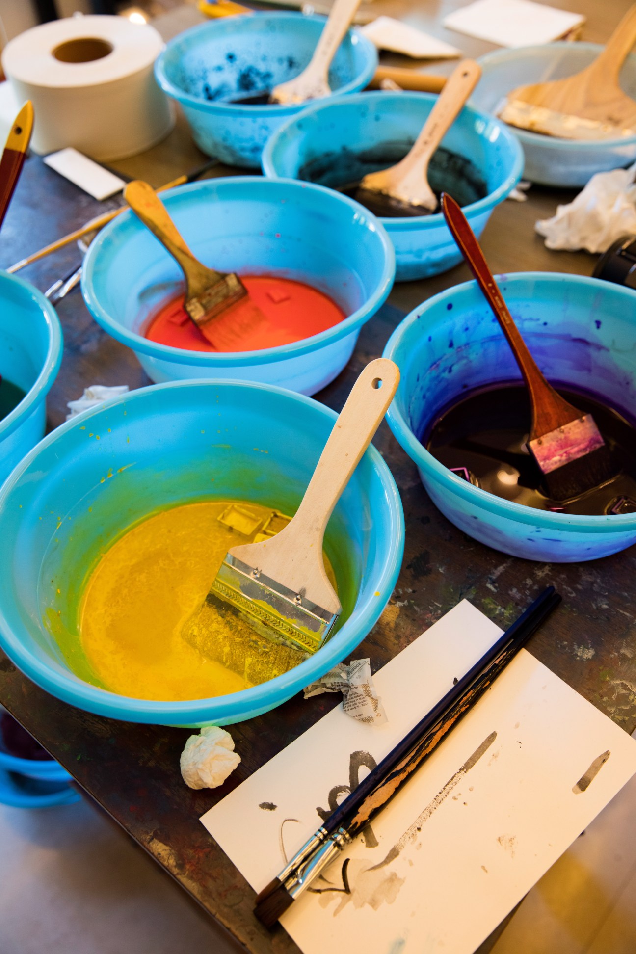 Artist's studio workspace with multiple blue bowls containing vibrant paint colors and brushes.
