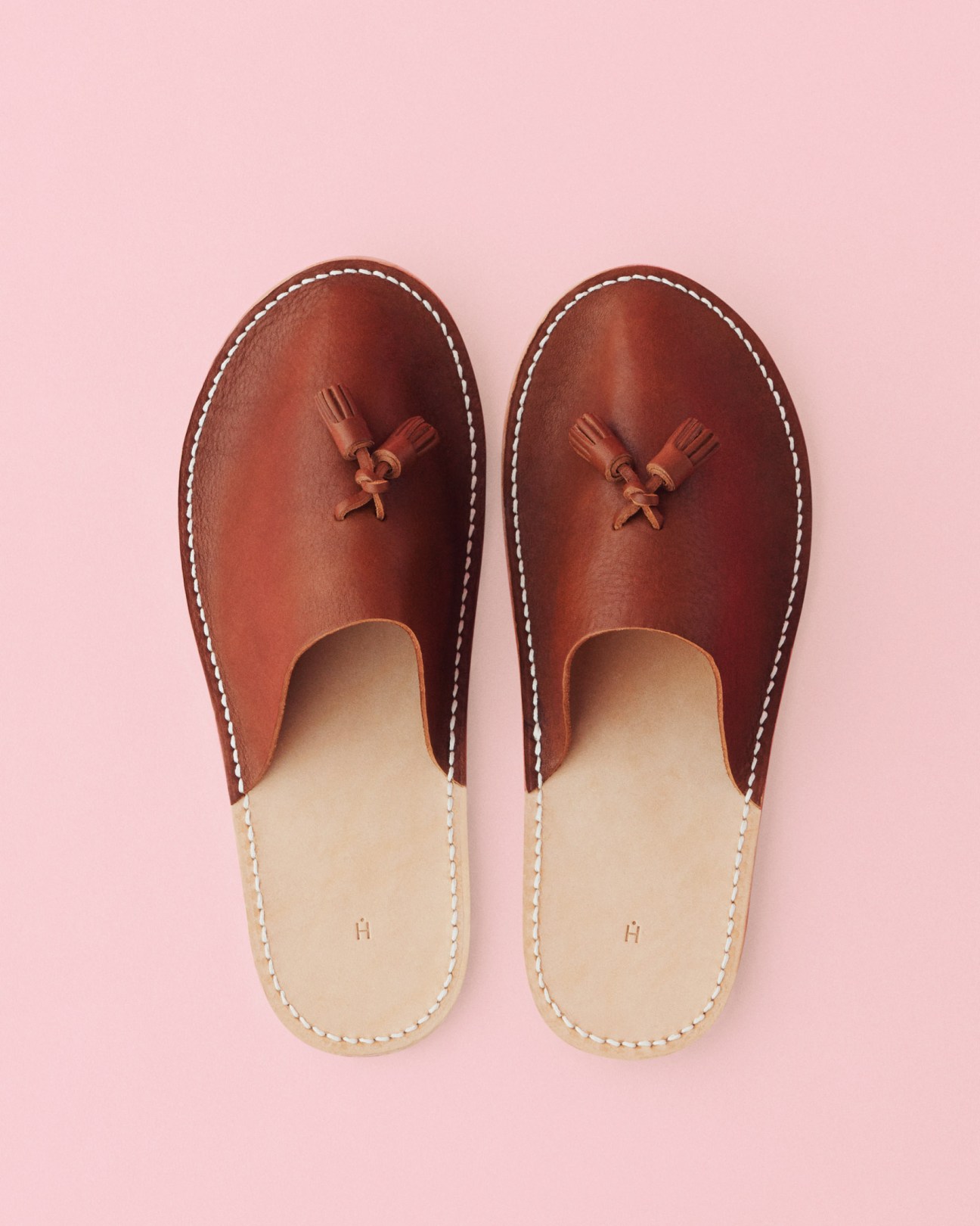 Pair of brown leather slip-on shoes by Hender Scheme with cream-colored soles on a pink background.