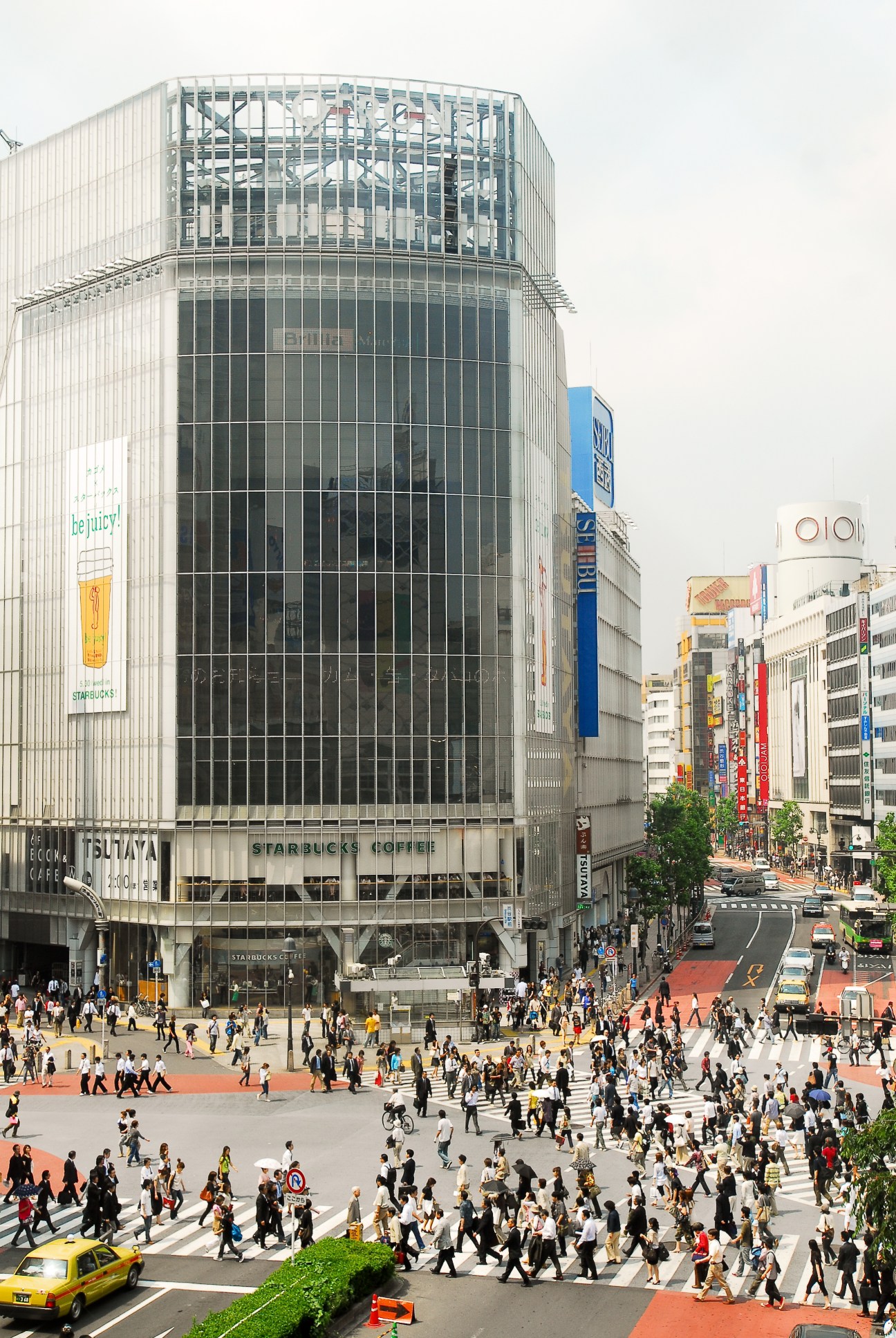 Busy pedestrian crossing with tall Starbucks building and commercial storefronts in urban cityscape.