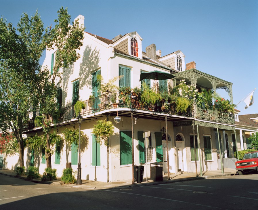 Historic white building with green shutters and wrought iron balcony in New Orleans French Quarter.