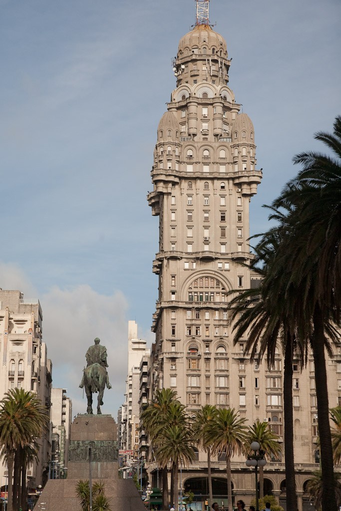 Palacio Salvio, a tall beige neoclassical building with a domed tower, stands prominently in Montevideo's cityscape flanked by palm trees.