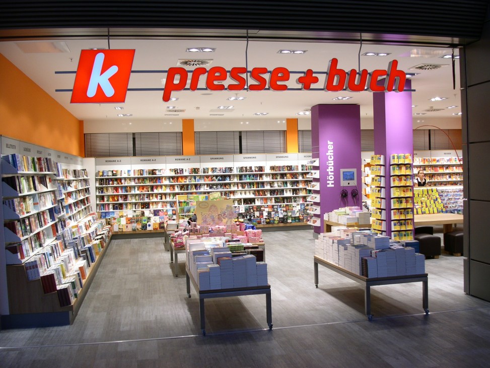 K Presse + Buch bookshop storefront at Hamburg airport with red signage and colorful interior displaying magazines and books.