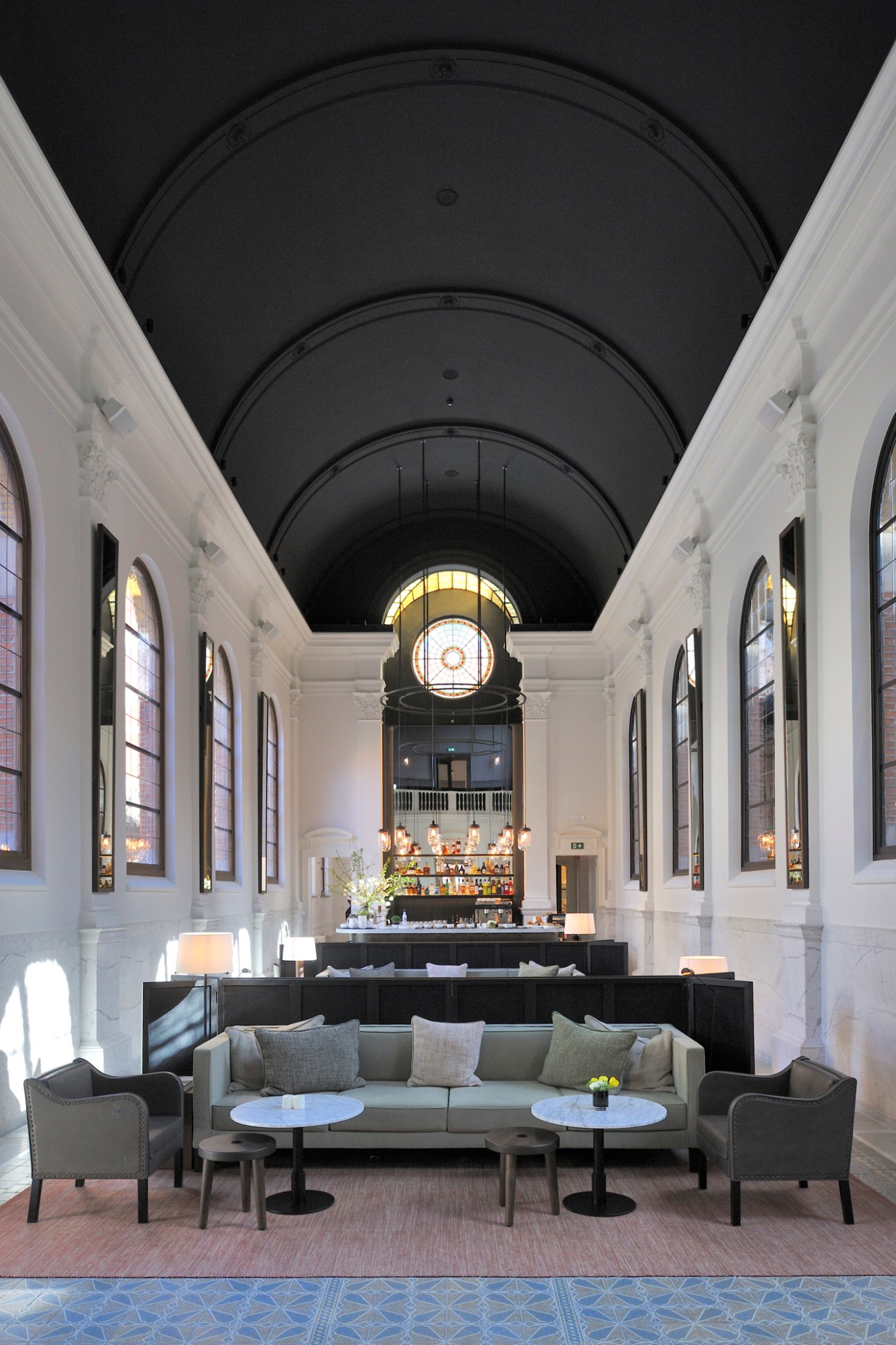 August hotel bar in converted Antwerp convent with arched ceiling, white walls, and modern furnishings.