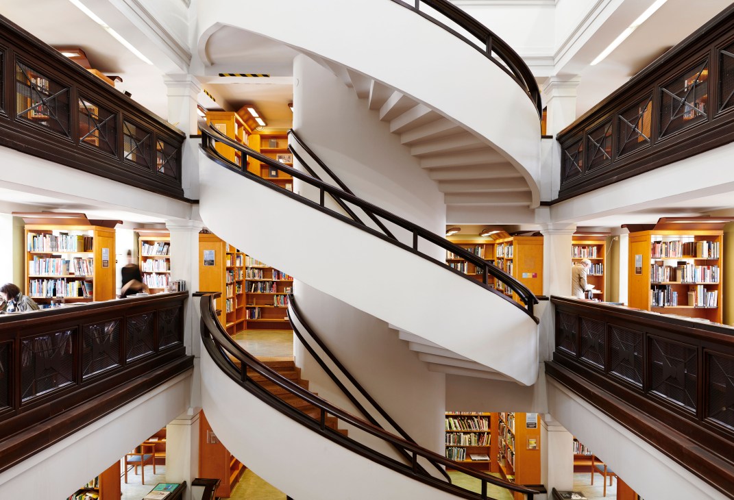 Multi-level Finnish library interior with spiral staircase, wooden shelving, and natural lighting