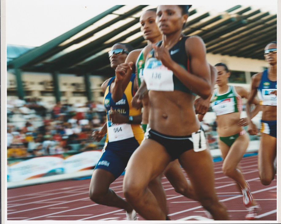 Female track athletes running in a women's 100m race at a stadium during the Jogos da Lusofonia.