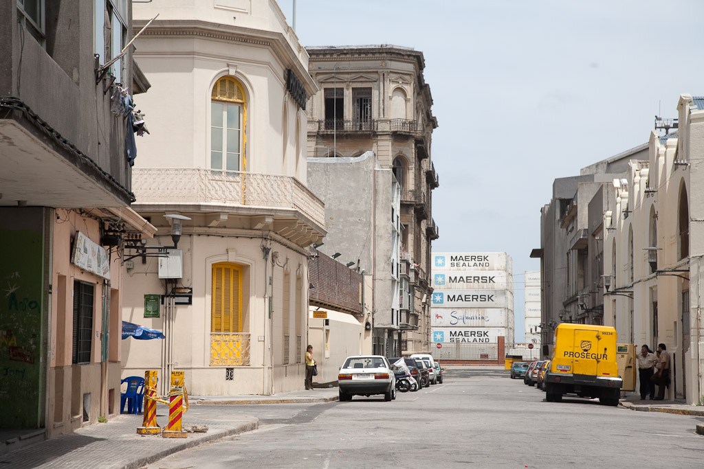 A street in Montevideo's Old City with colonial architecture, shipping containers, and parked vehicles.