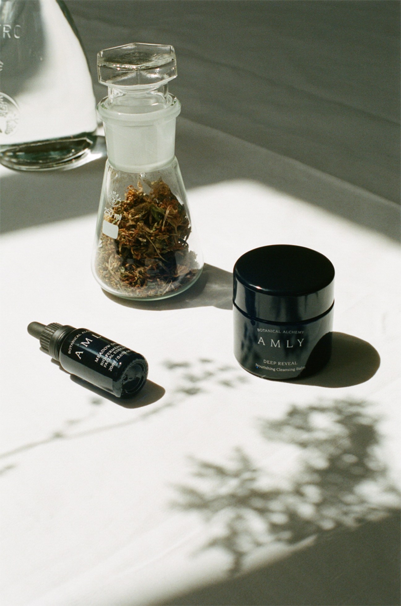 Amly skincare products displayed with dried botanicals in a glass jar.