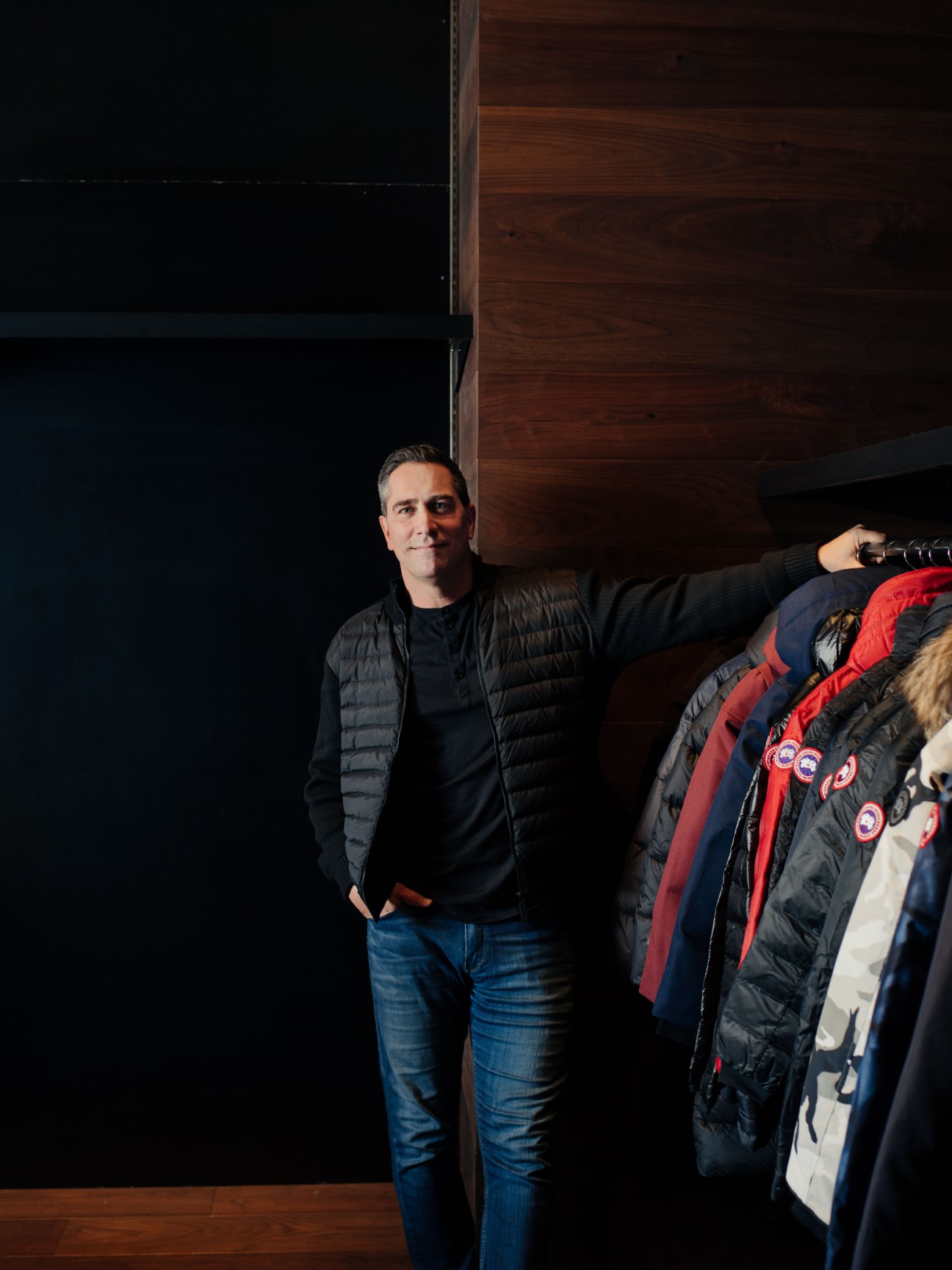 Pat Sherlock stands next to a display of Canada Goose parkas in various colors including red, navy, and black.