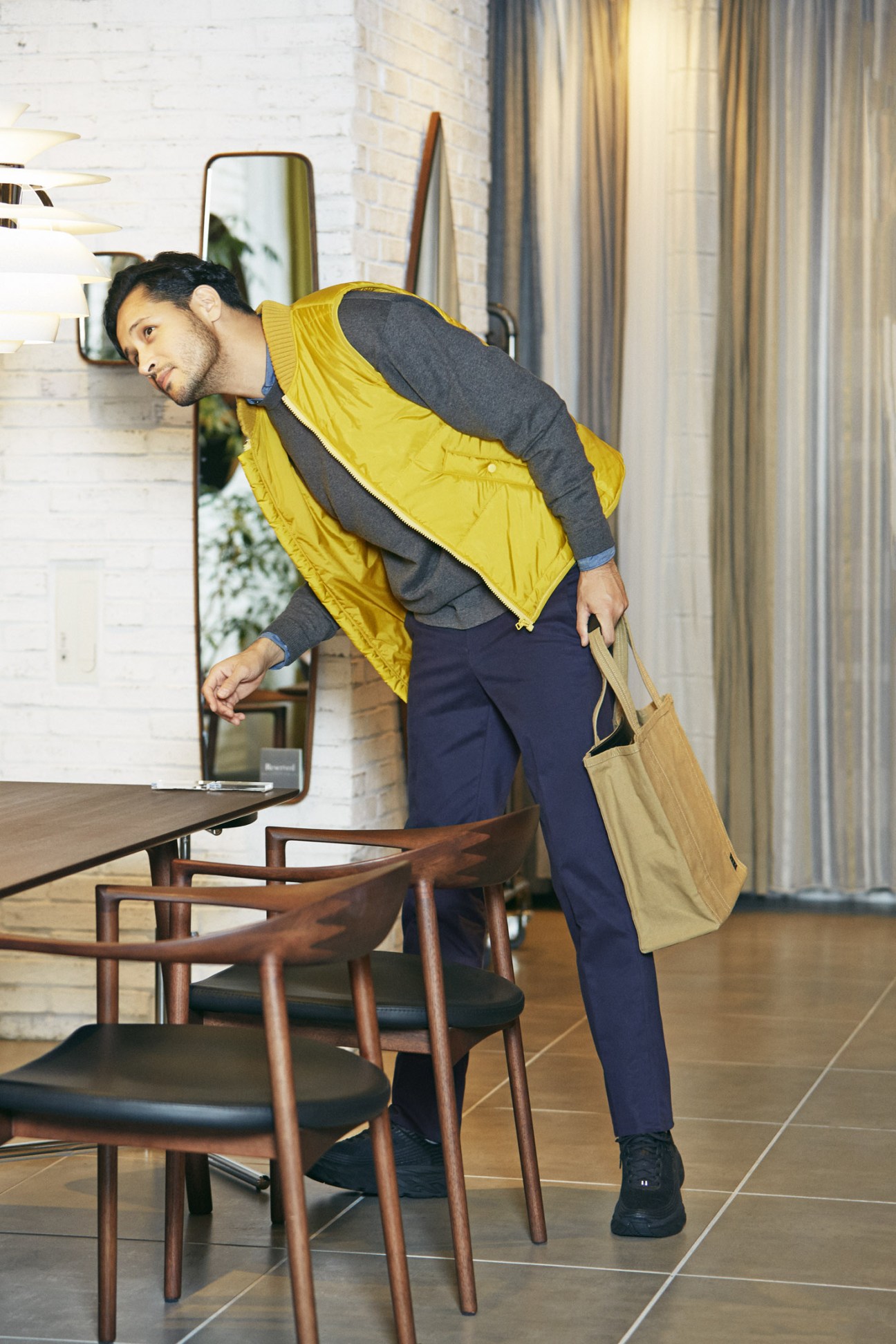 Man in yellow gilet and navy trousers carries Porter bag in modern interior with Actus dining furniture