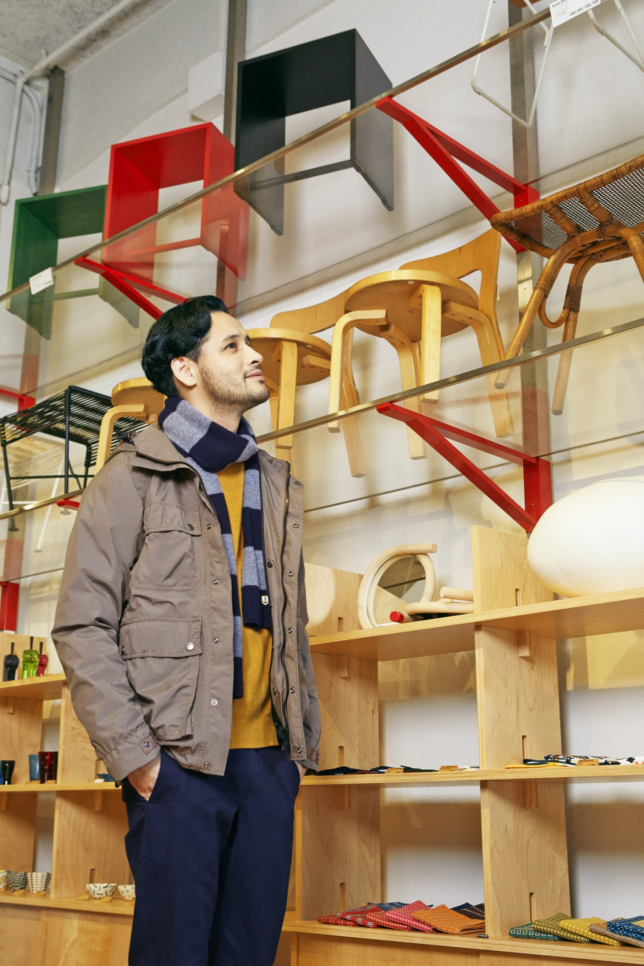Man wearing Woolrich jacket, Adam Et Ropé jumper, A Kind Of Guise trousers and Armor Lux scarf in modern furniture showroom.