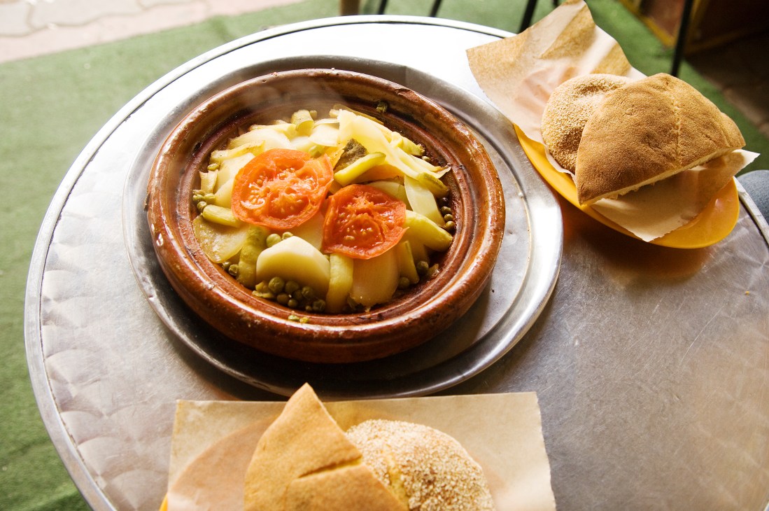A traditional Moroccan tagine stew in a clay pot with vegetables and bread on the side.