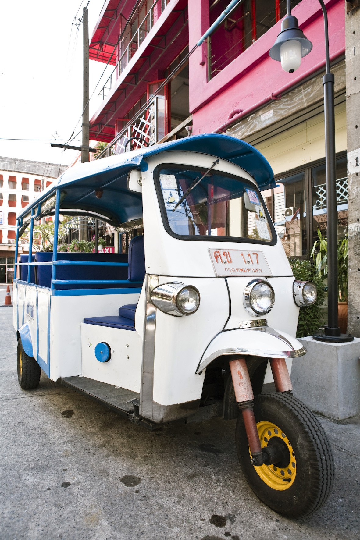 White and blue tuktuk parked on a Bangkok street with colorful buildings in background.