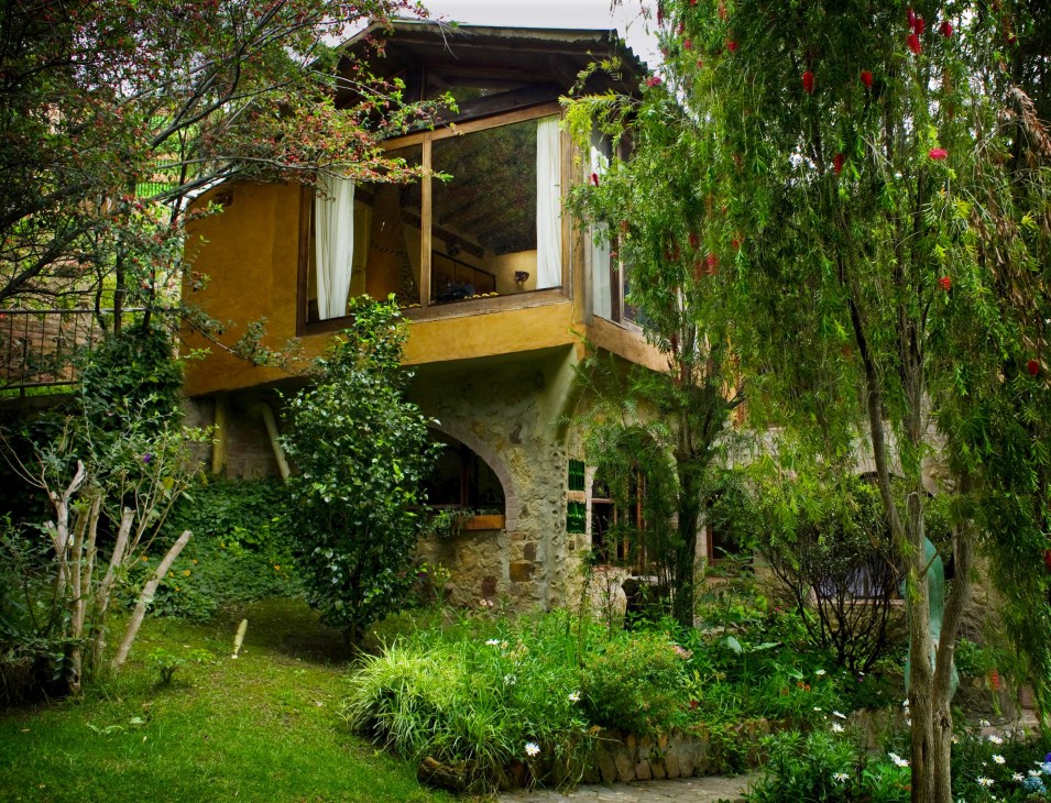 Yellow-painted house surrounded by lush green vegetation and flowering vines in Villa de Leyva countryside.