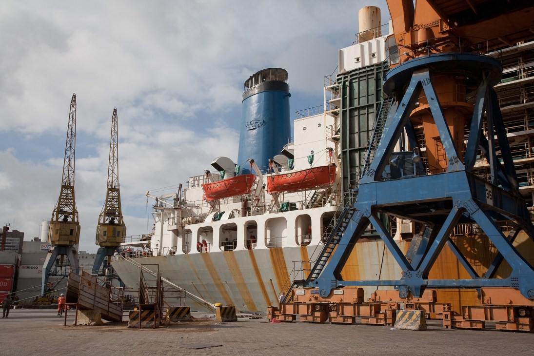 Industrial cargo ship docked at Montevideo's port with loading cranes and equipment.