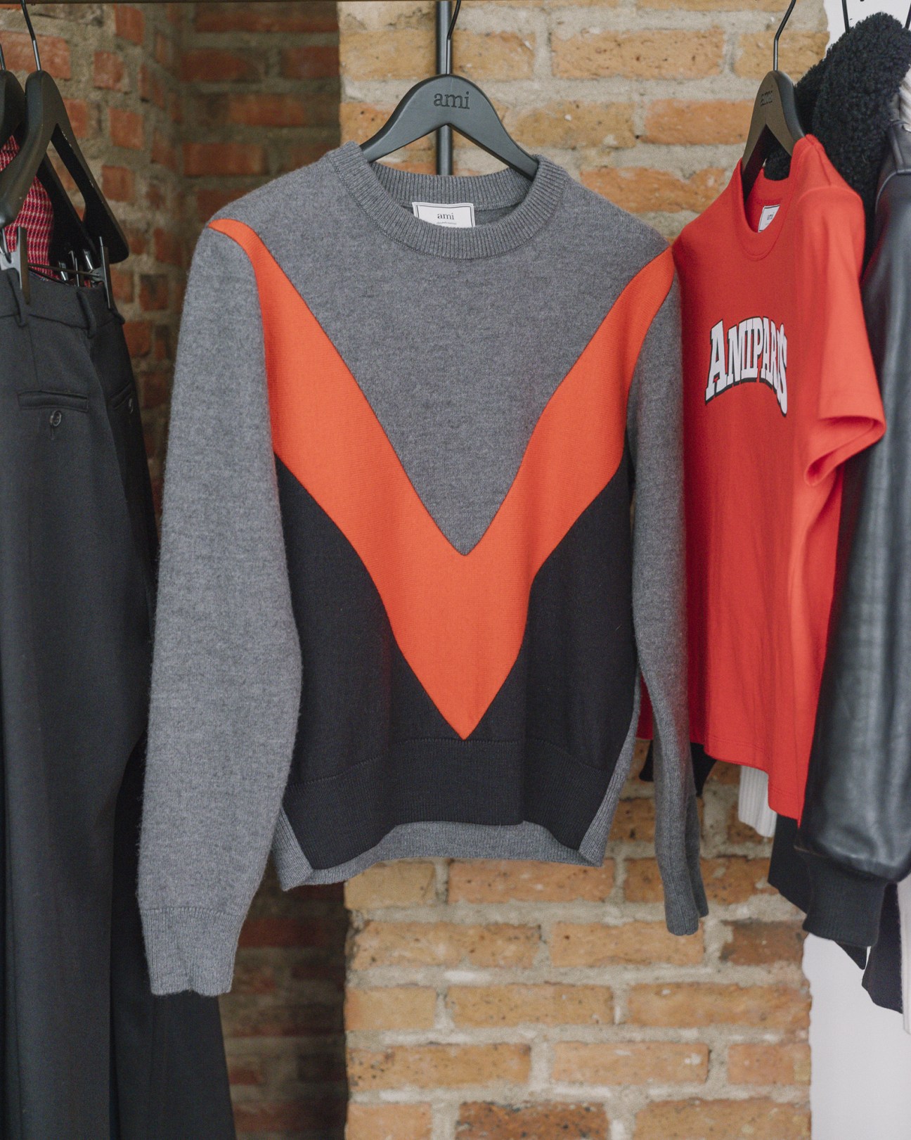 Ami sweater with gray and black colorblock design and orange V-stripe on display hanger.