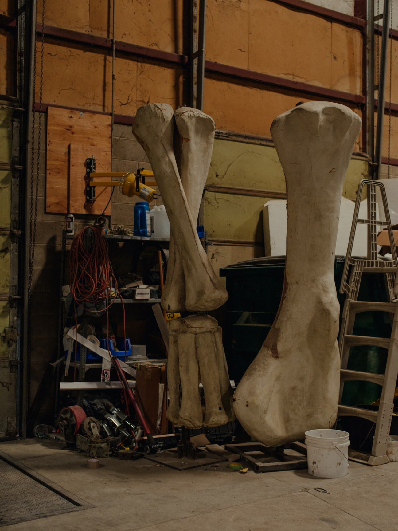 Large white dinosaur bone casts standing upright in an industrial workshop with tools and equipment