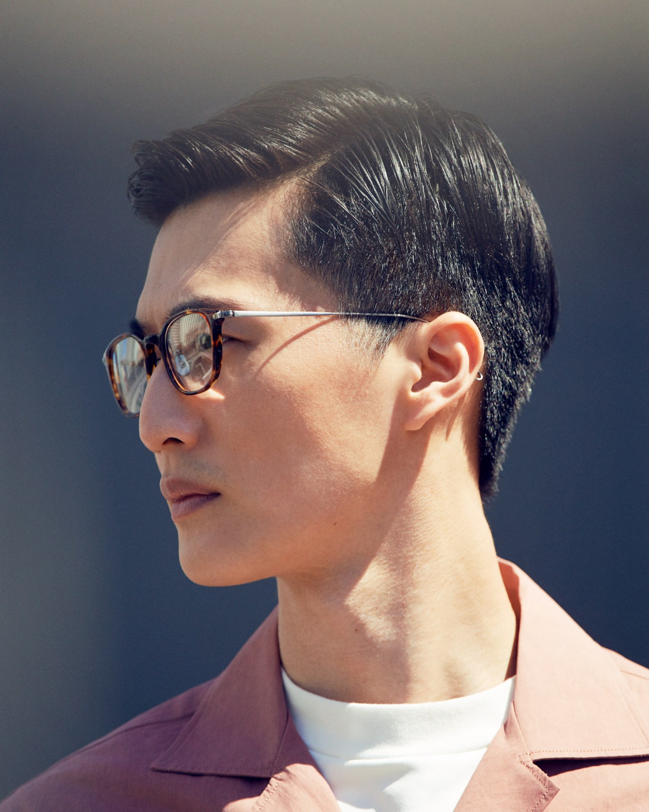 Man in profile wearing tortoiseshell glasses, white t-shirt and pink shirt by Studio Nicholson and Scye.