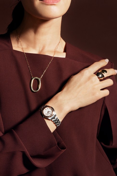 Person in cream sweater with jewelry and watch against white background