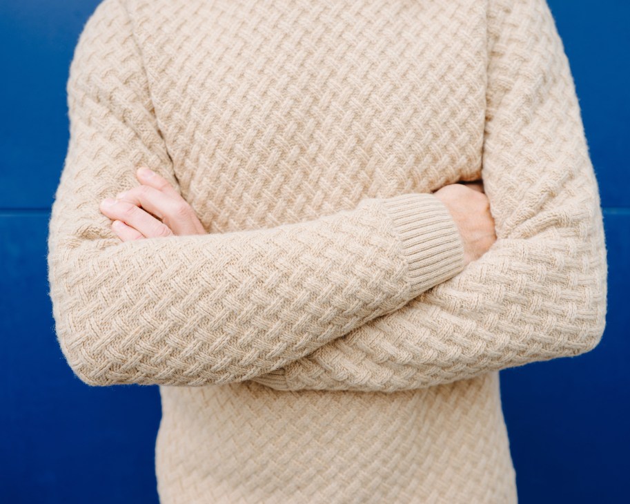 Person wearing a cream-colored textured knit sweater against a blue background.
