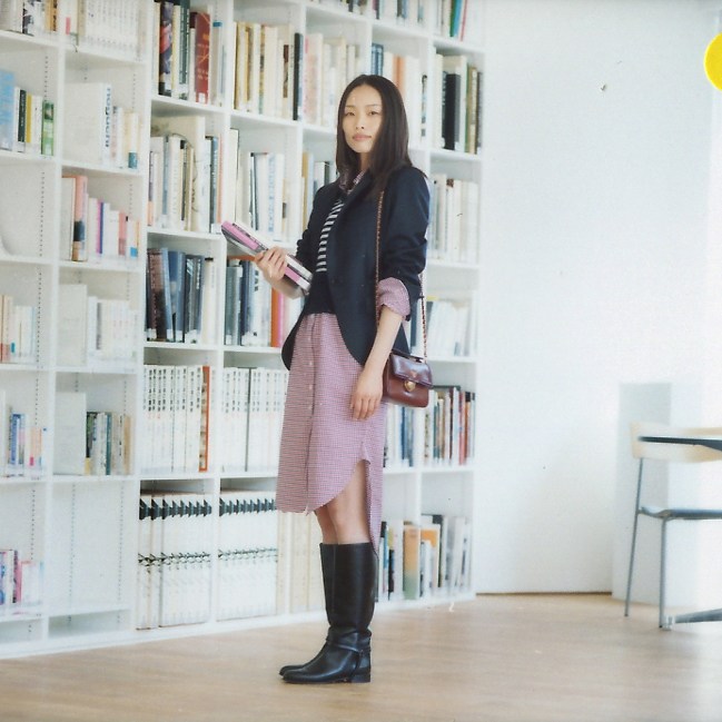 Woman in business attire posing in front of library shelves holding a pink folder.