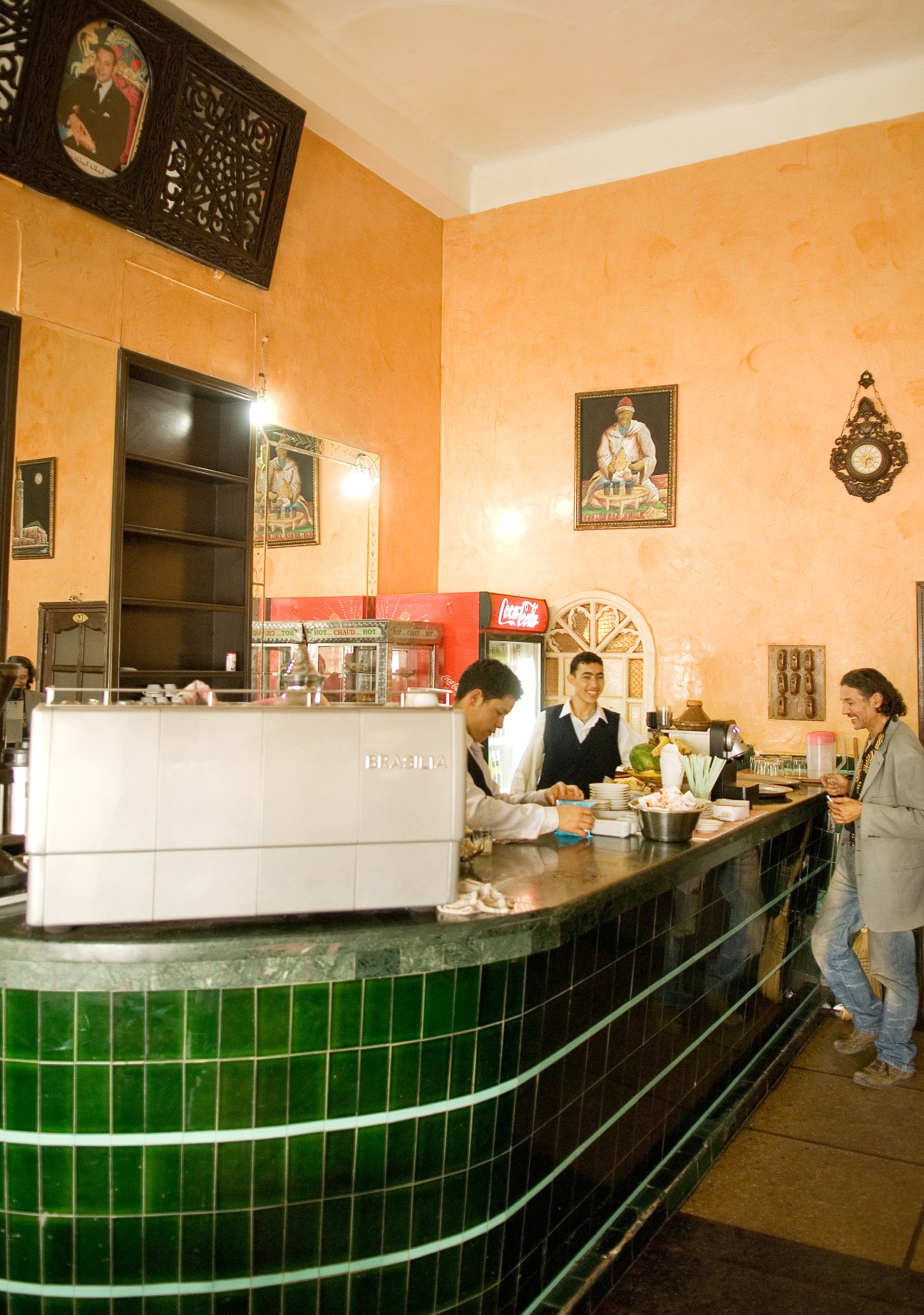 Moroccan café counter with staff and customer in traditional interior with orange walls and green tilework.