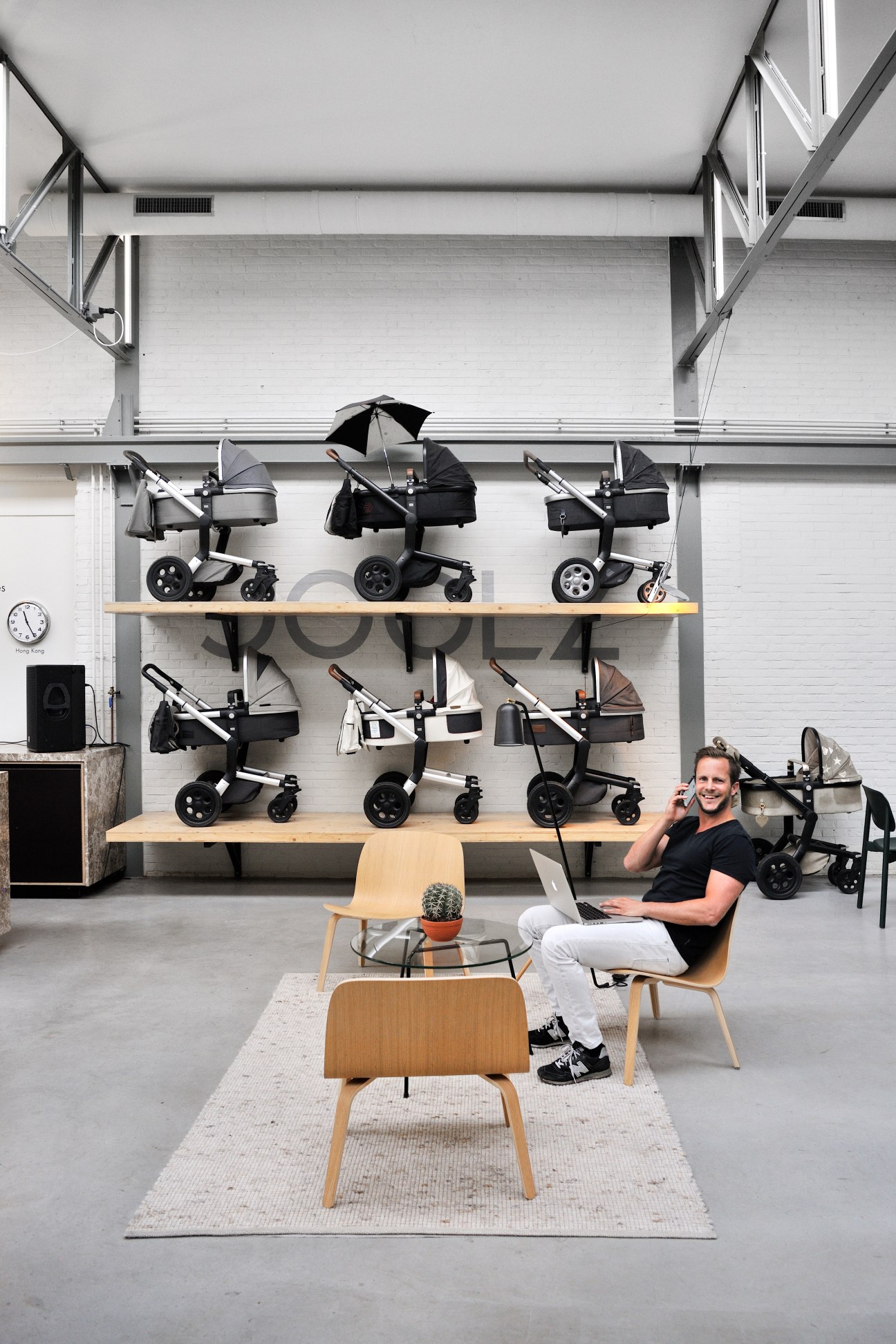 Man sitting in wooden chair with laptop in modern office space with baby strollers displayed on wall shelves