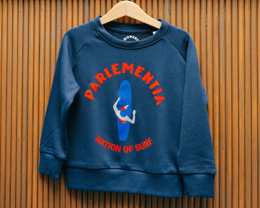 Navy blue Parlementia sweatshirt with red and blue surf graphic on wooden background.