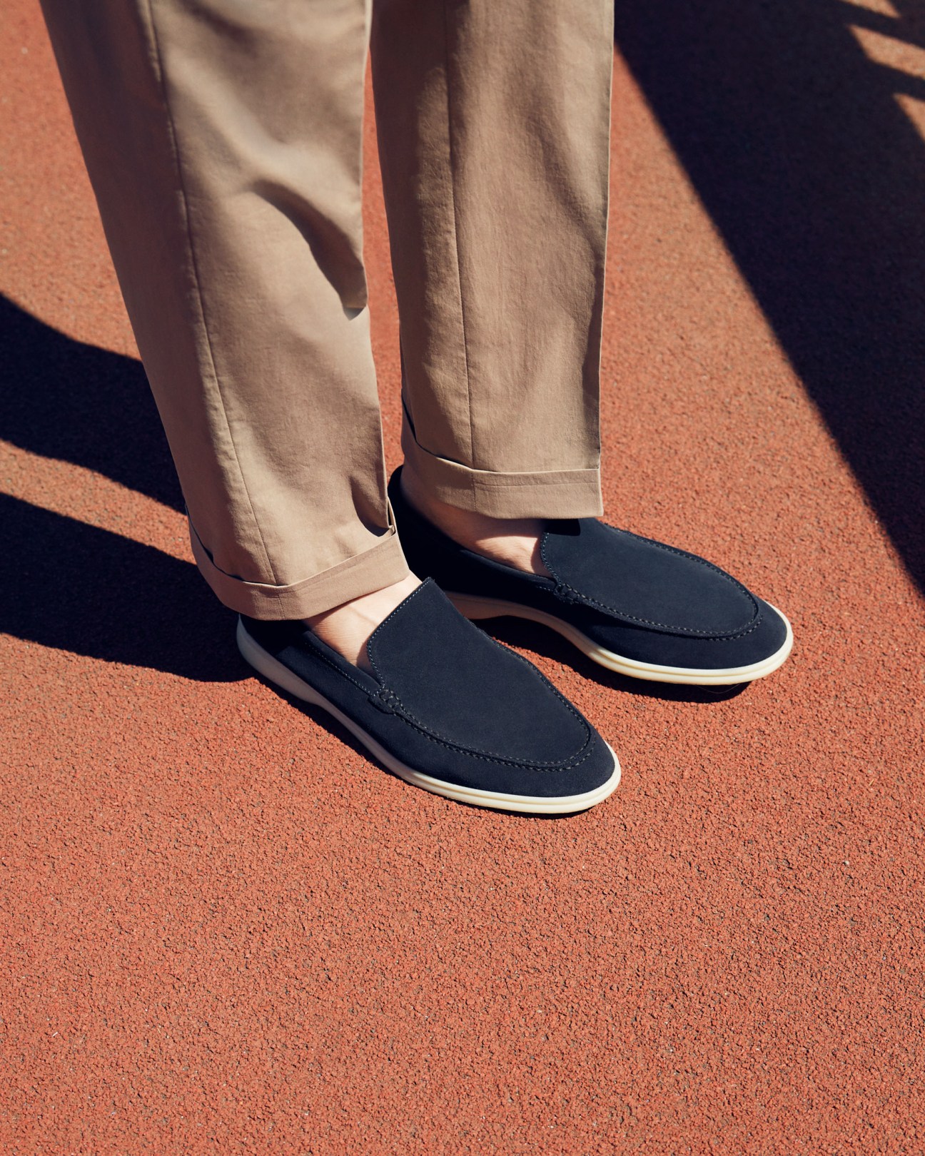 Close-up of beige rolled trousers and navy slip-on shoes on an orange surface.