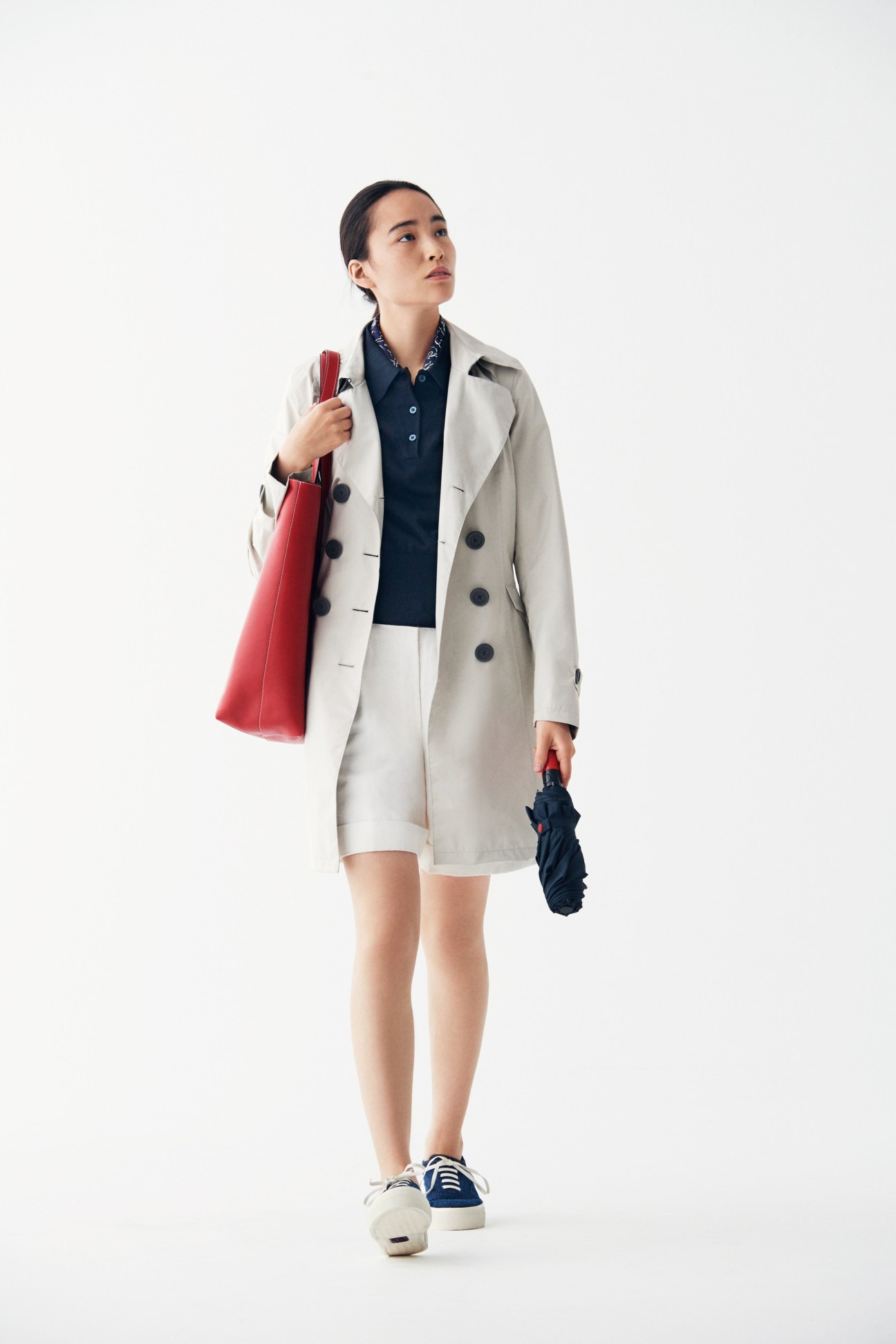 Woman in cream-colored coat by Sealup and navy polo shirt holding a red Prada backpack.