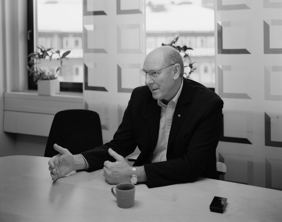 Gert-Inge Andersson, Trollhättan's mayor, gestures while speaking at a table in an office with geometric patterned windows behind him.