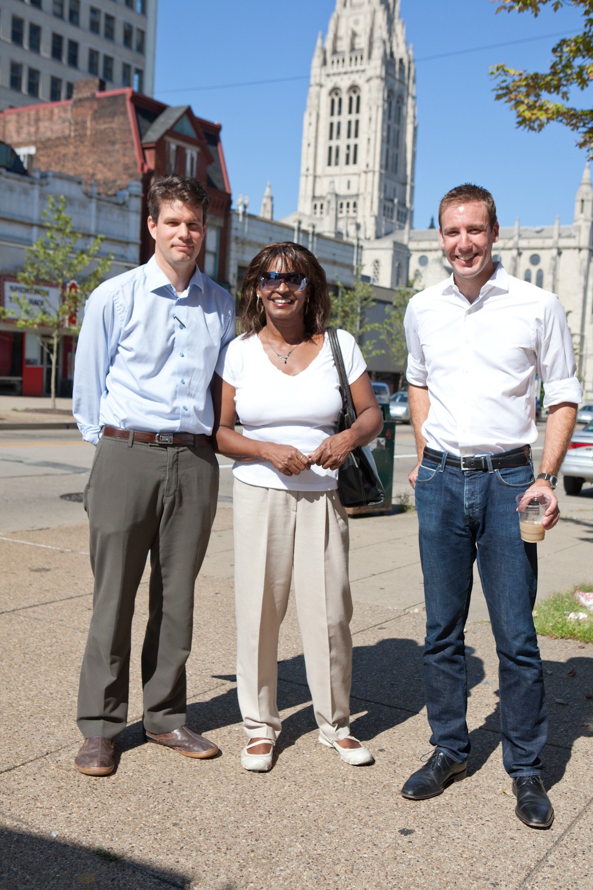 Three professionals stand on a Pittsburgh street with a Gothic cathedral visible in the background.