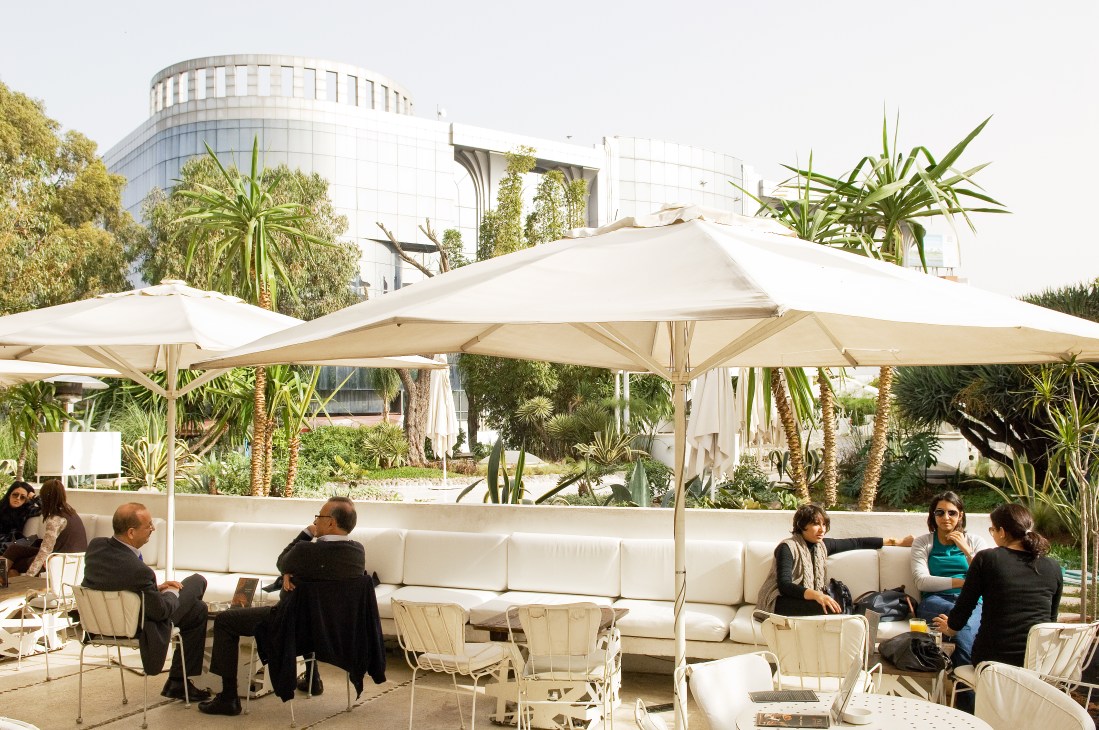 Outdoor terrace seating at Paul Villa Zevaco with white umbrellas, palm plants, and modern architecture.