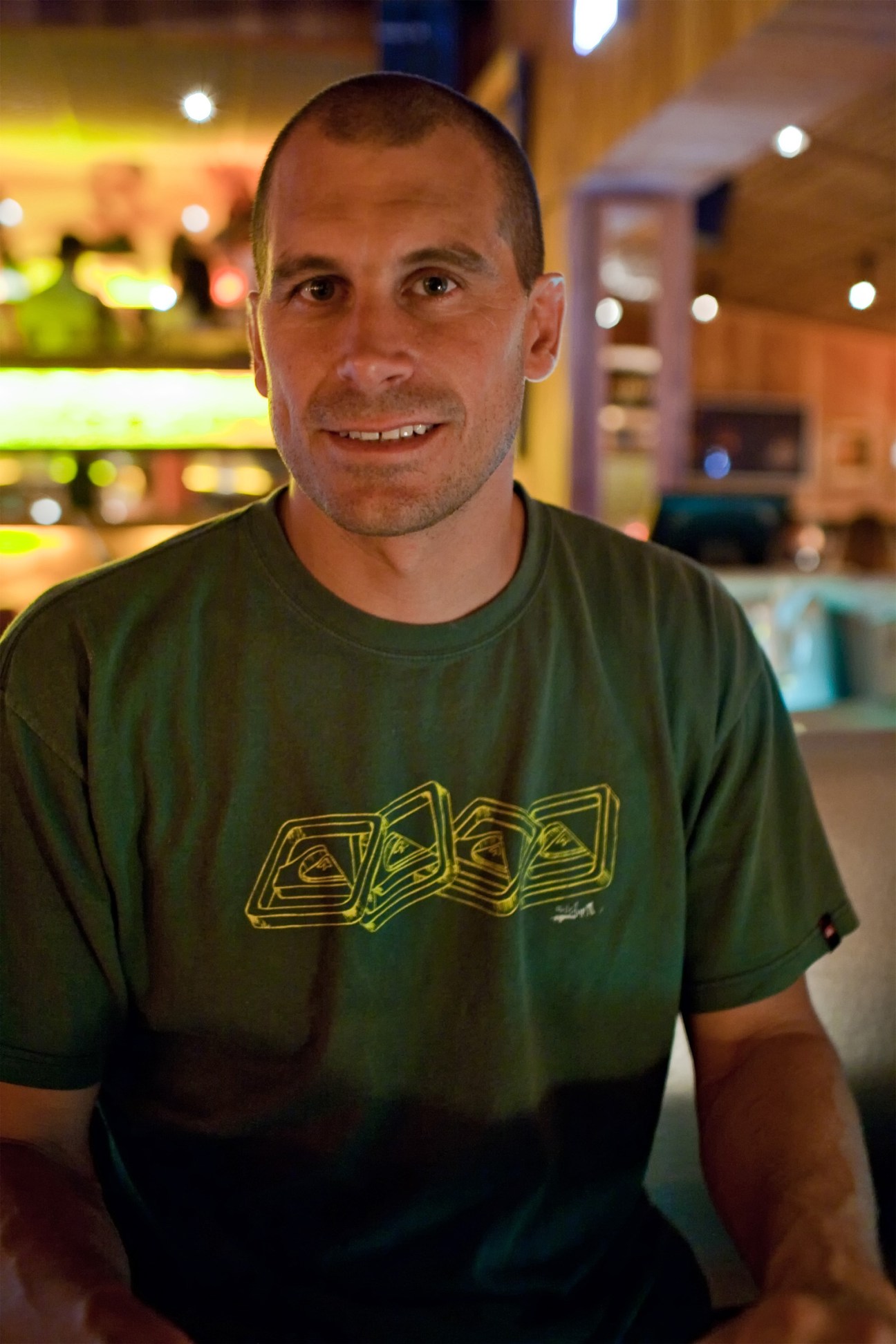Juan Pablo Clerici, co-owner of Café Misterio, smiles at the camera in a green graphic t-shirt.