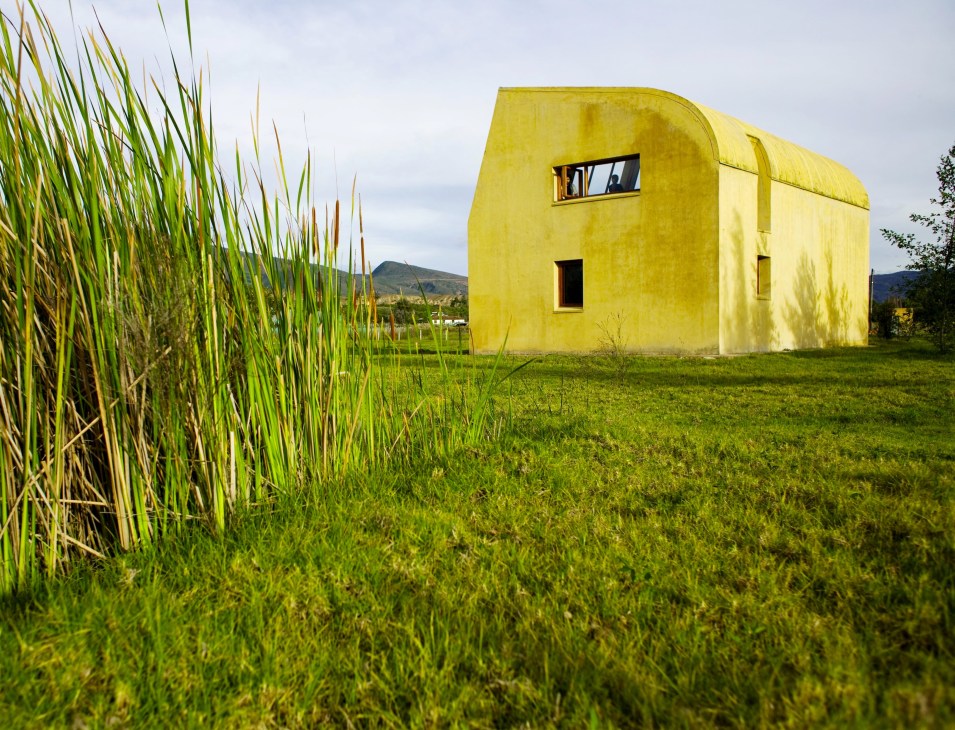 Bright yellow modern house with curved walls in green countryside near Villa de Leyva, Colombia.