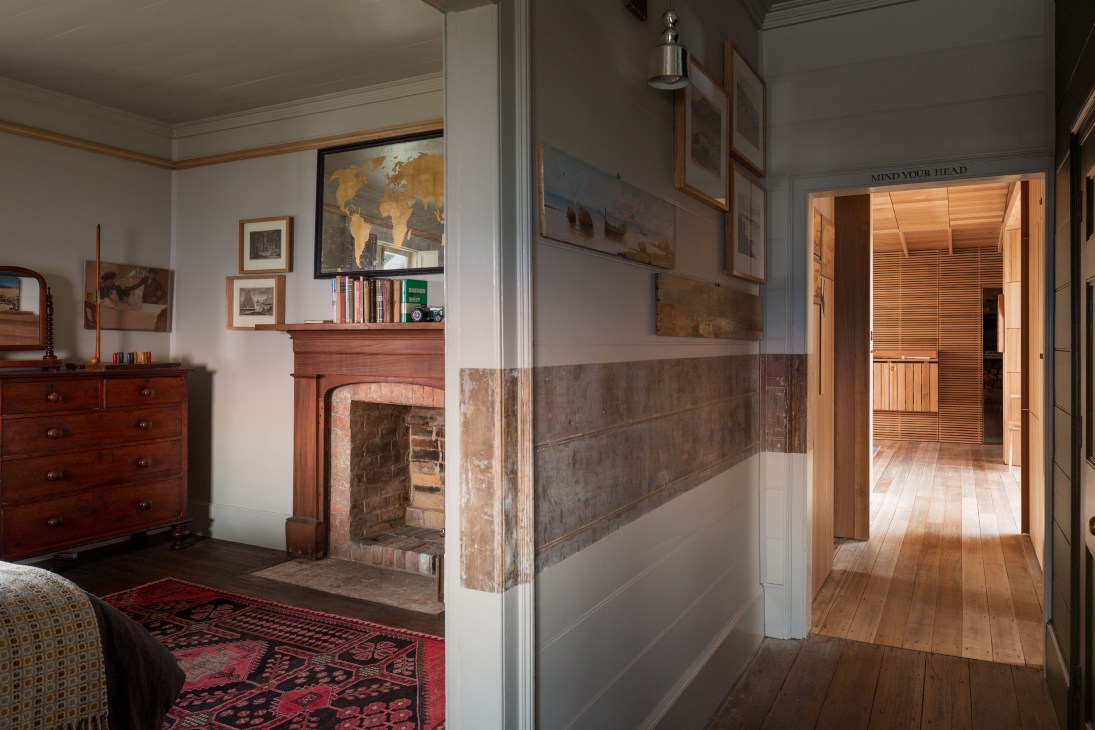 Interior hallway of restored cottage showing central passage with exposed brick fireplace, wooden floors, and "Mind your Head" sign.