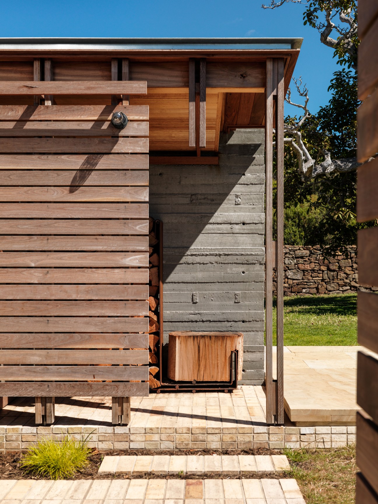 Exterior view of a wooden cottage with horizontal timber cladding and a concrete doorway, showing an axe handle used as a doorknob.