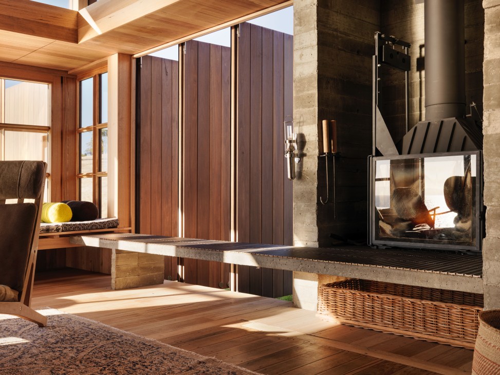 Modern living space with wooden ceiling and walls, retractable dark shutters, concrete fireplace recess, and sunlit window seat.