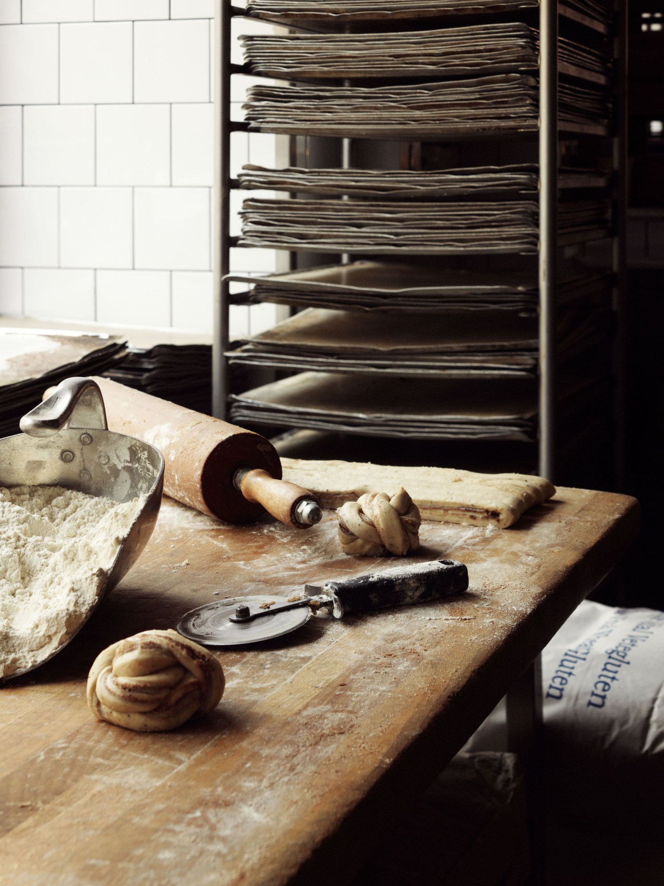 Bakery tools and a pastry on a wooden work surface with baking sheets in the background.